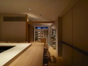 A well-lit dining space with a long wooden table surrounded by chairs, bottles, and a warm ambiance