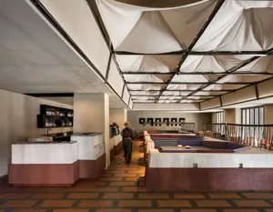 A casual restaurant with a dining table, chairs, and bottles, featuring a person walking through the space, with a focus on socializing and enjoying food and drinks in a comfortable environment