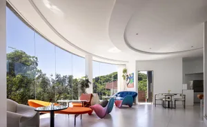 Open modern living space with white walls, wood furniture, and natural light from a large window