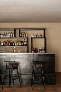 Modern bar area with a black countertop, stools, and bottles on display
