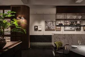 A clean and organized interior design showroom with white walls, framed pictures, a potted plant, and two chairs