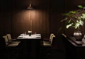 Dark dining area with wooden walls and tables, four chairs, and wine glasses, creating an intimate and cozy ambiance