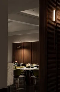 Warm and inviting restaurant interior with wooden walls and floors, multiple dining tables, chairs, potted plants, and vases