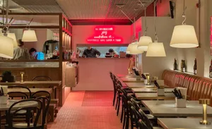 A warm and inviting restaurant interior with red accents, pink and white tiles, and dining tables with chairs and bottles