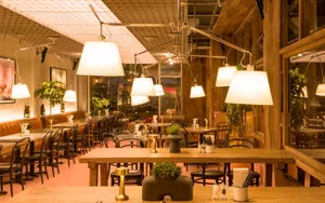 Dimly lit restaurant interior with wooden tables, chairs, potted plants, and hanging lamps