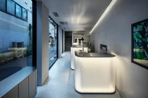 A modern restaurant interior with white walls and floors, featuring two large countertops, chairs, and a dining table, creating a clean and simple atmosphere