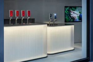 Modern bar area with white countertops, beverage dispensers, and cups, set in a stylish and upscale environment