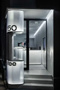 A modern industrial cafe with concrete walls, a counter area, and a black door leading outside, featuring a coffee machine and cups on the countertop