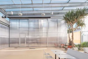 a contemporary living space with a glass wall, metal frame, chairs, and a dining table