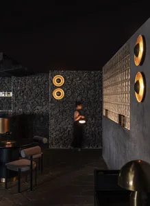 A cozy bar area with a woman standing near a wall, two chairs, and a dining table, featuring wooden accents and a warm atmosphere