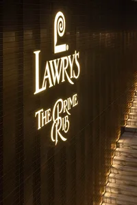 A well-lit restaurant with a gold sign reading Lawry's Prime Rib on a black background, visible through windows