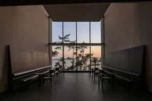 A serene waterfront building with multiple windows, benches, and a sunset view