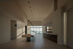 Open living area with white walls and floors, featuring chairs, a dining table, and a clock on the wall, creating a spacious and inviting atmosphere