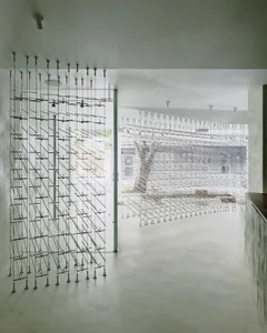 A modern open-plan living area with a kitchen, featuring a wire mesh door, a tree trunk, and a minimalist atmosphere