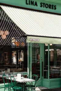 A restaurant interior with multiple tables, chairs, and people, featuring green accents on the walls and flooring, and warm lighting creating a comfortable ambiance