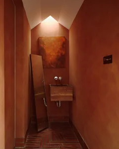 A bathroom with an orange color scheme, brick-patterned walls, a wooden sink countertop, and a mirror above the sink