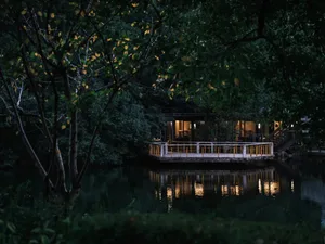 A serene Asian-style house near water with a wooden structure, yellow accents, and a balcony overlooking the water