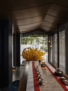 A cozy dining area with a long wooden table, red tablecloth, and chairs, featuring cups, bowls, and vases arranged on the table