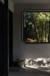 A serene Asian-style room with a gray wall, a window with bamboo plants outside, and two potted plants in front of the window
