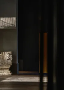 A stone statue on a pedestal in a museum-like space with a neutral color palette and subtle lighting