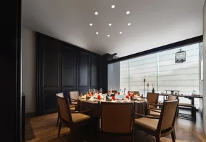 Dining area with a round table set with various items, surrounded by chairs, in a warm and sophisticated space with black and brown tones