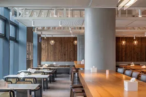 Empty restaurant with wooden floors and walls, featuring chairs around dining tables in a calm and inviting atmosphere