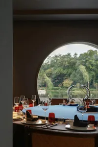A warm and inviting dining space with a round table, chairs, wine glasses, vases, and utensils, set in a restaurant-style interior