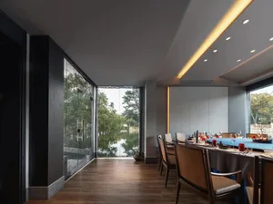 A modern dining area with a large table set with wine glasses, cups, and utensils, surrounded by chairs, on wooden floors, with a black wall in the background