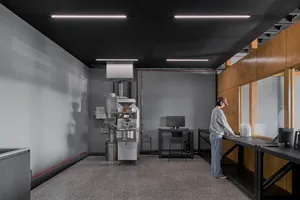 Industrial kitchen with functional layout, featuring machines, chairs, and a dining table, with a focus on efficiency and organization