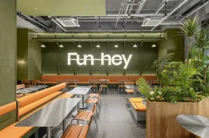 Casual dining space with a large green wall, chairs, and a potted plant, creating a welcoming atmosphere