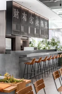 A modern Asian restaurant interior with a long metal counter and multiple chairs, gray and black elements, and a sleek atmosphere