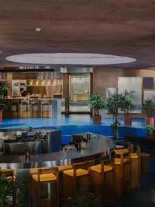 Modern restaurant interior with a circular bar, wood accents, metal elements, and potted plants, creating an inviting and comfortable atmosphere
