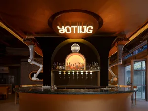 A modern bar with a wooden wall, featuring a large counter with numerous bottles and beer taps, creating a relaxed and social atmosphere