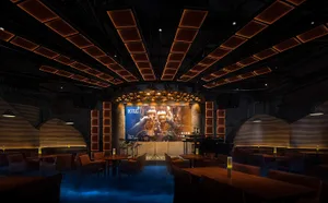 A lively bar with a stage in the center, surrounded by chairs and a dining table, creating a social gathering atmosphere