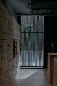 A hotel lobby with stone walls, a large window, and a doorway leading outside, featuring a bench for seating