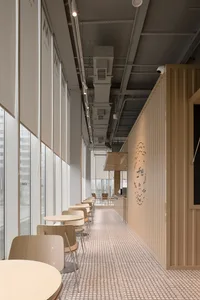 A well-lit restaurant with a long dining table and comfortable seating, surrounded by wooden furniture and possibly natural light