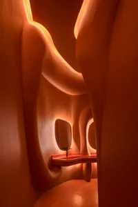 A serene bathroom interior with a red countertop, stone walls, and a sink, set in a museum or gallery space