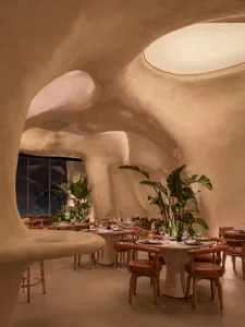 A modern restaurant interior with a large dining area, potted plants, artwork on the walls, and warm lighting