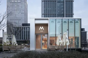 A modern cafe with a glass front facade, comfortable seating area with chairs and umbrellas, and an inviting atmosphere