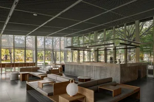 Modern restaurant with concrete walls, seating areas, and dining tables, lit by lamps