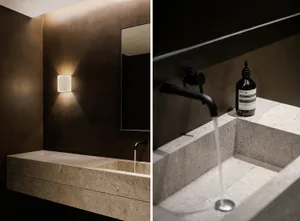 Bathroom with stone surfaces, sink basins, faucets, and a mirror, with bottles placed nearby