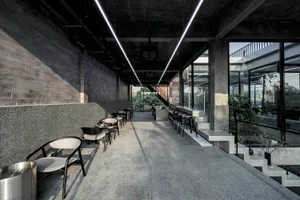 Spacious modern lobby with concrete floors and walls, featuring seating areas with chairs and dining tables, and an inviting atmosphere