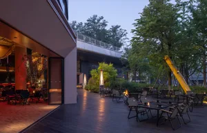 A restaurant patio at night with tables, chairs, umbrellas, candles, and a bridge, featuring wood flooring and a warm atmosphere