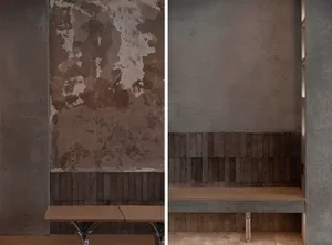 A rustic dining space with a stone wall, wooden benches, and a dining table, featuring peeling paint on the wall and a brown color scheme