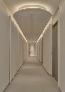 一條長形現代走廊，擁有白色牆壁與地板，設有多扇門，以及一位站在相鄰房間的人