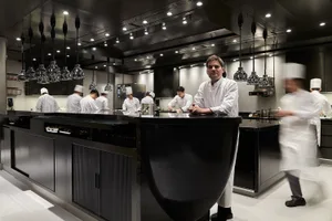 A bustling commercial kitchen with a black countertop island, multiple appliances, and several people working together