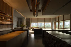 A modern kitchen with a large dining table, black countertops, appliances, and potted plants, creating a contemporary and inviting atmosphere