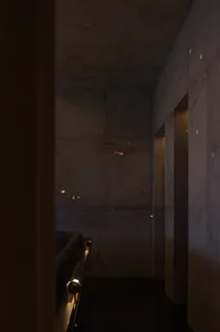Dark living room with a couch in the corner, two benches, and dim lighting, featuring concrete walls