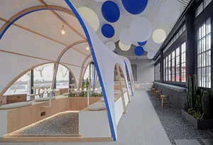 Open restaurant interior with multiple tables, chairs, potted plants, and round balls hanging from the ceiling
