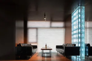 A modern living room with two black leather couches, chairs, a dining table, and a bottle on a table, surrounded by large windows